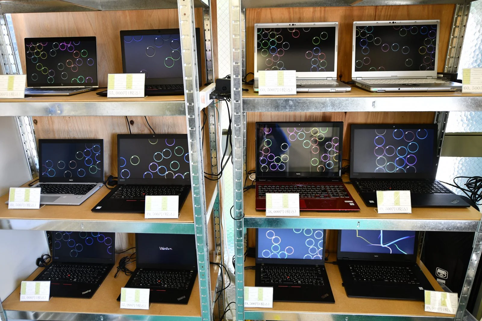 パソコンショップエムズの在庫棚。中古ノートパソコンを1台ずつ通電した状態で展示している